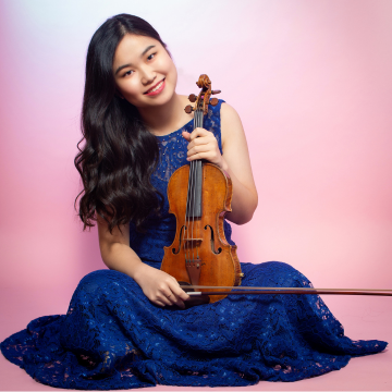 SooBeen Lee sitting on the floor with her legs crossed in a blue dress holding a violin.