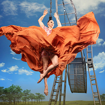 Cirque Mechanics in Zephyr aerialist midair in a billowing orange dress