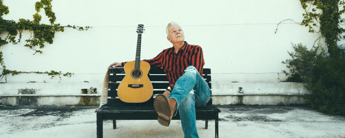 Tommy Emmanuel sitting on a bench with a guitar