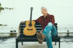 Tommy Emmanuel on a bench with a guitar