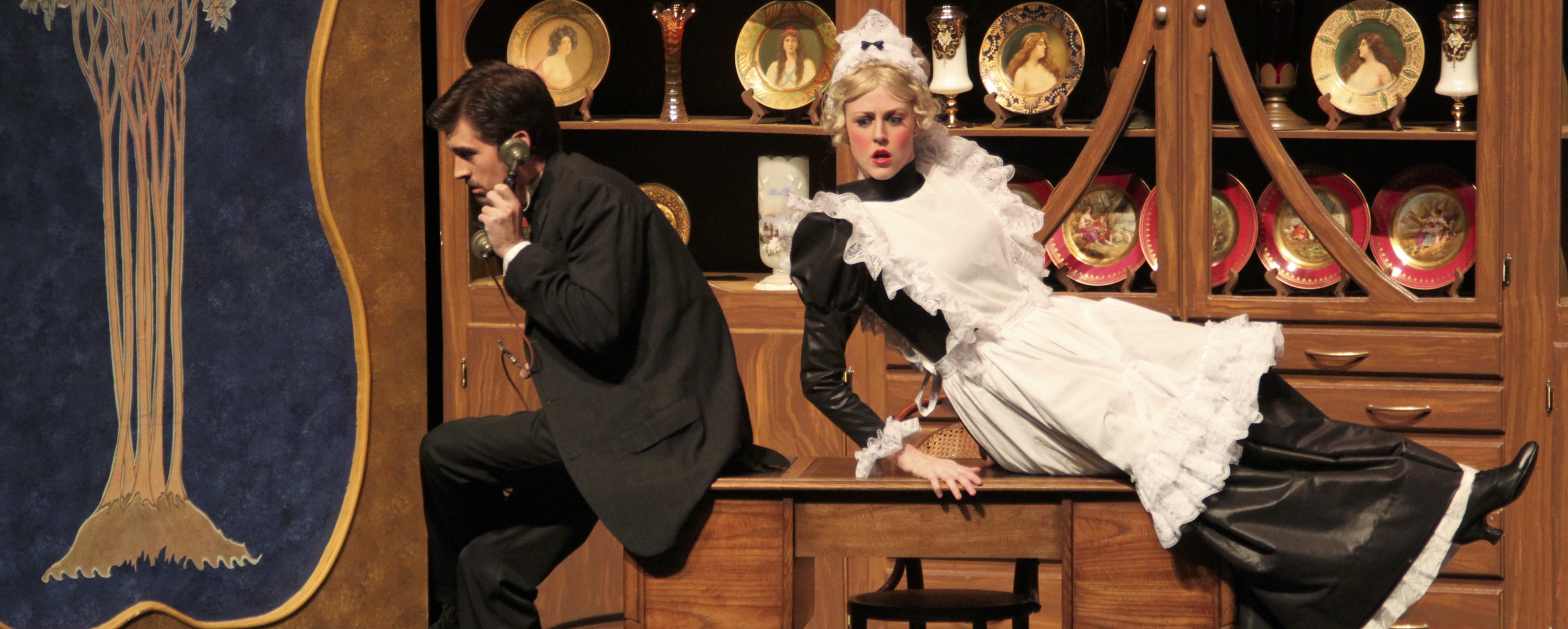 Image of a maid sitting across a table listening to a man who is on the phone