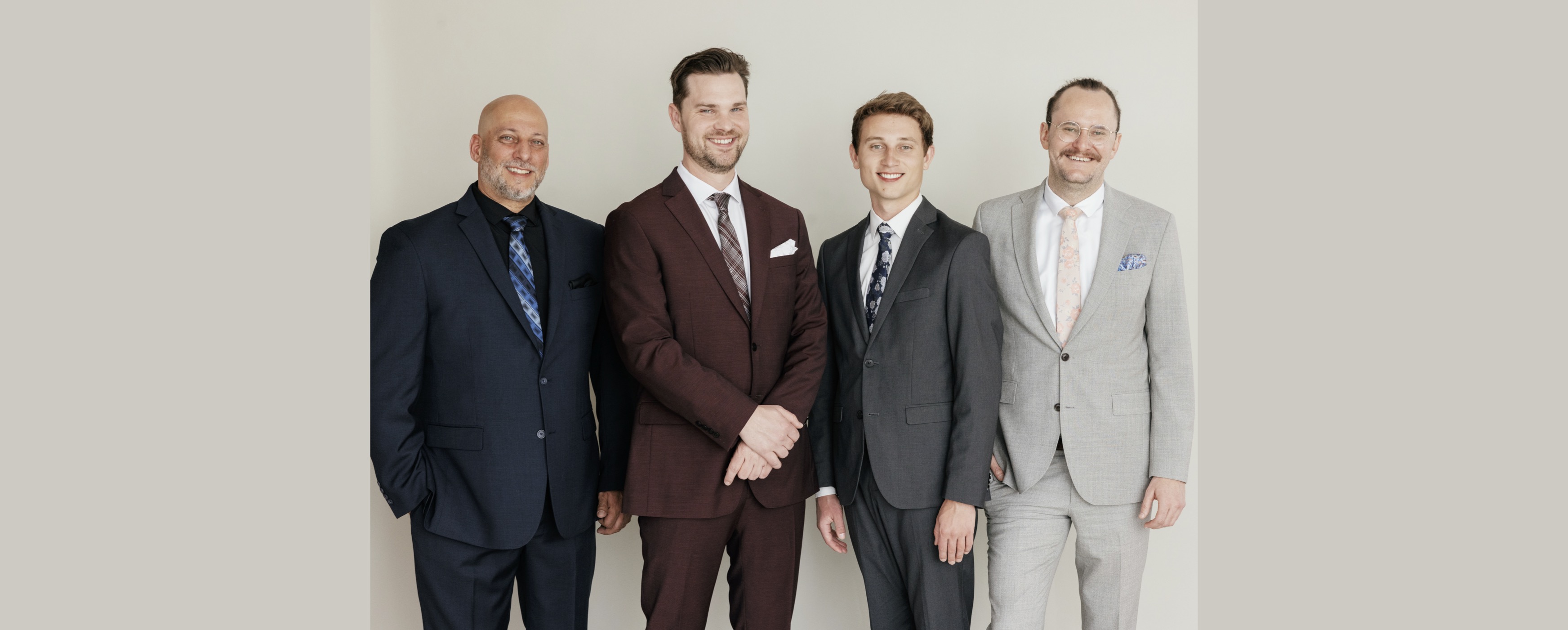 Image of four happy men in suits in front of blank wall