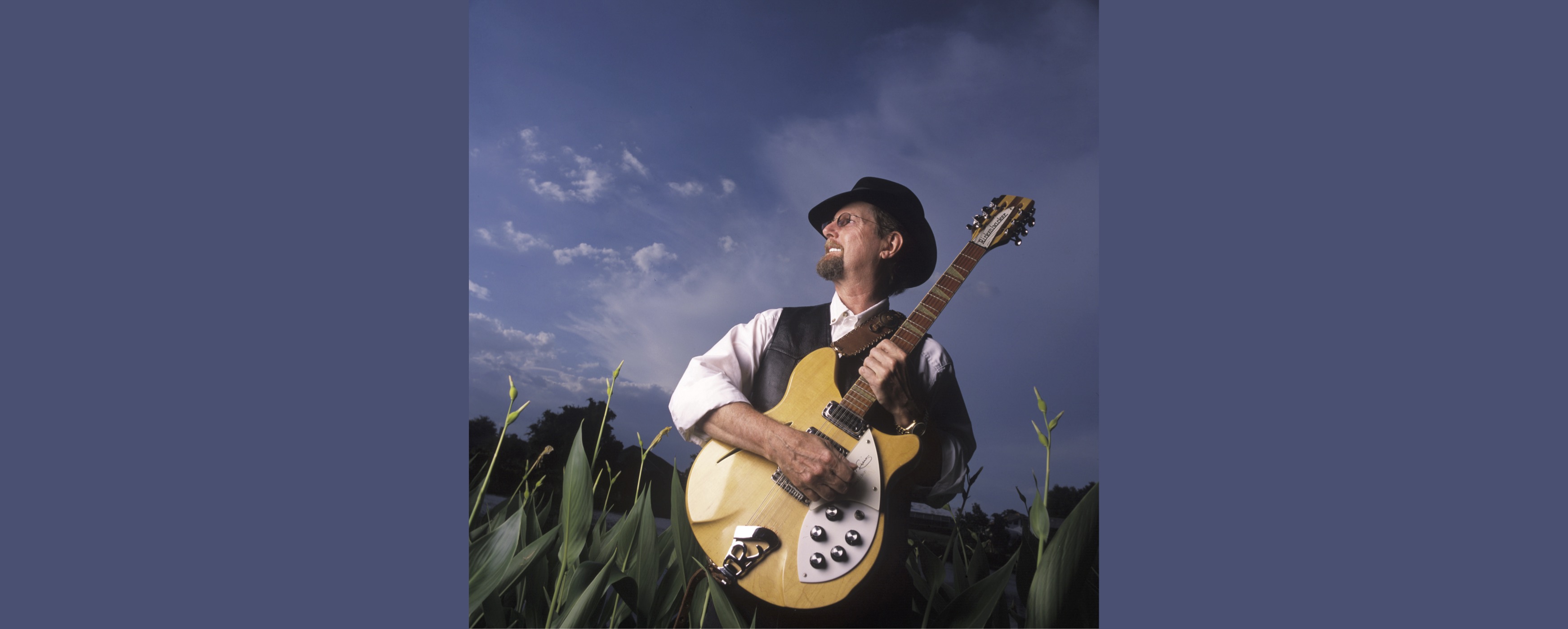 Image of Roger McGuinn with guitar in front of blue sky