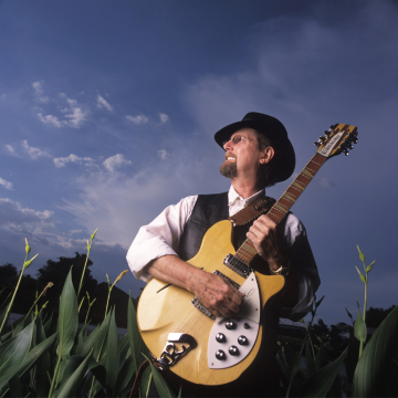 Image of Roger McGuinn with a guitar in a field 